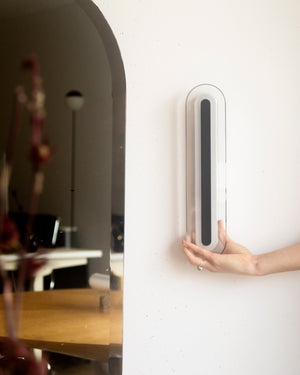 A hand holding a slim, vertical wall light in a living room