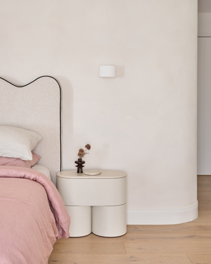 Blanco Interiors Project: A modern bedroom scene featuring a low, cylindrical nightstand with an up down plaster wall light.