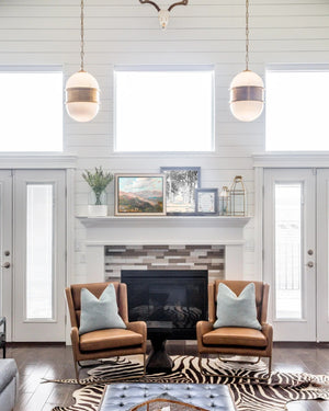 Pair of brass capsule pendants suspended above fireplace seating in bright shiplap living room interior