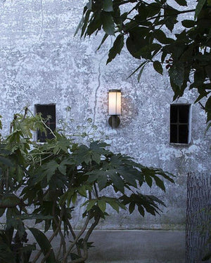 Brass Lantern Wall Light mounted on aged stone exterior wall at dusk casting warm glow through frosted glass cylinder