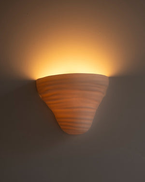 ceramic wall sconce mounted on white wall with warm light on 