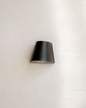 Conical indirect step light in antique brass mounted on a white textured wall