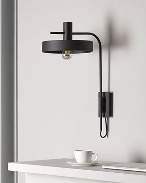 Modern black wall lamp on a white wall with a cup and saucer on a table below.