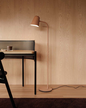 Modern floor lamp with a wooden desk and chair against a wooden wall.
