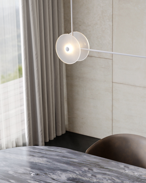 Modern pendant light hanging above a marble table with a neutral wall and curtain in the background