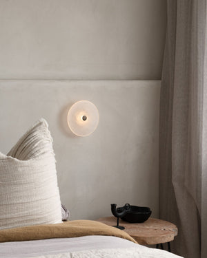 Wall-mounted light fixture on a neutral wall with a pillow and decorative item in the foreground.
