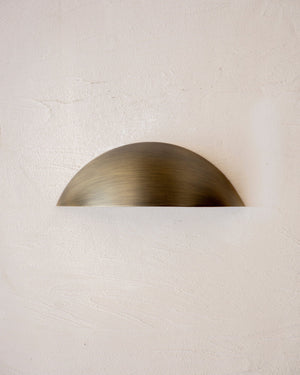 Curved outdoor step light in antique brass finish mounted on a white textured wall
