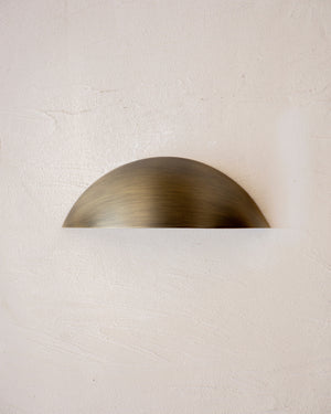 Curved outdoor step light in antique brass finish mounted on a white textured wall