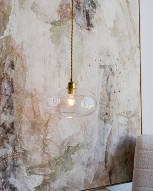 Pendant light with a glass shade against a textured wall.