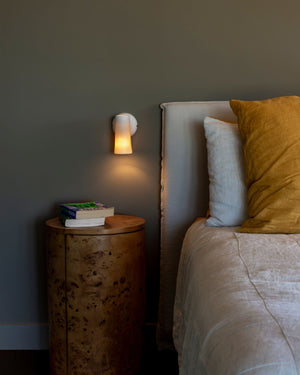 Bedroom with a bedside table and white wall lamp next to a bed with pillows.