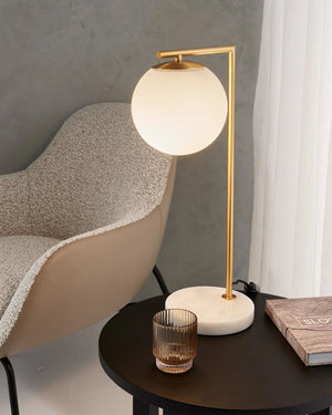 Modern table lamp with a round glass shade on a dark surface next to a textured chair.