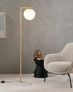 Modern floor lamp with a spherical light bulb next to a textured armchair in a room with gray walls and a white floor.