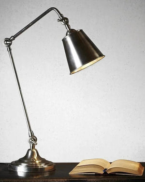 Vintage-style desk lamp with adjustable arm on a wooden surface next to an open book.