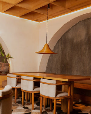 A brown reed pendant light suspended above a wooden dining table in a warm interior