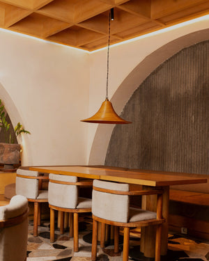 A brown reed pendant light suspended above a wooden dining table in a warm interior