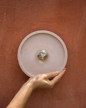 Person holding a round light fixture against a red-brown wall