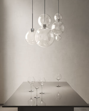 Glass sphere ceiling lights suspended above a metal table in a dining room space with wine glasses on the table