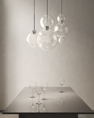 Glass sphere ceiling lights suspended above a metal table in a dining room space with wine glasses on the table