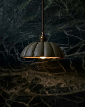 Floral Concrete Pendant Light in moss finish suspended and lit against dark green marble wall