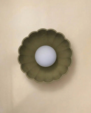 A scalloped, flower-shaped wall sconce in a muted olive green shade