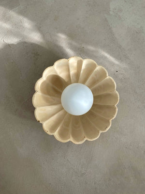 Floral Concrete Wall Sconce in sand finish with opal globe sphere on textured plaster surface with natural light and shadow