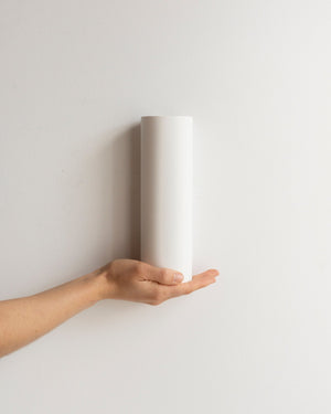 A hand holding a flush up and down plaster wall light tricolour against a white wall
