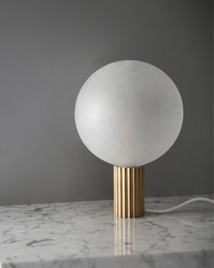Table lamp with a white spherical shade and gold base on a marble surface.