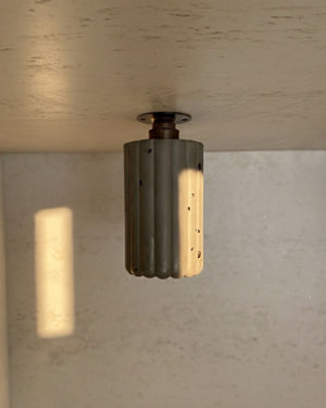 Fluted Concrete Downlight in moss finish with antique brass fitting mounted to render ceiling, lit with warm downward glow