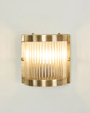 Fluted glass brass wall light illuminated showing warm glow through vertical glass rod diffuser and antique brass frame
