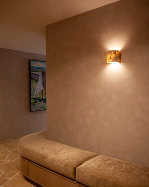 A warm coral wall sconce mounted on a textured beige plaster wall