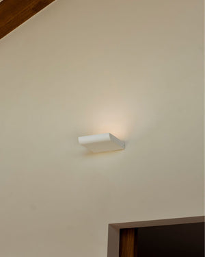 Square uplighter on a beige wall with a wooden baseboard.