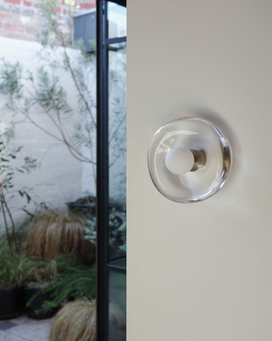 Handmade glass wall sconce on a white wall with a garden in the background 
