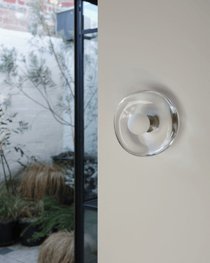Handmade glass wall sconce on a white wall with a garden in the background 