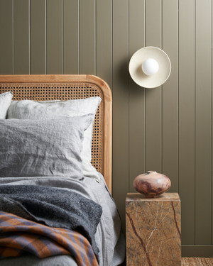 Bedroom with wooden headboard, gray bedding, and a wall sconce on a green paneled wall.