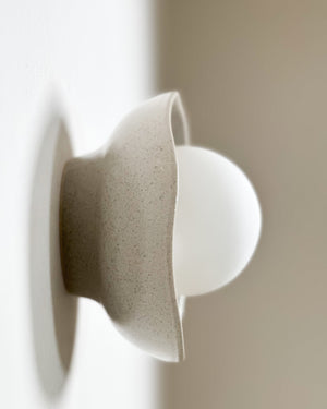 Shale glazed ceramic shell sconce with spherical bulb mounted on white wall side angle view