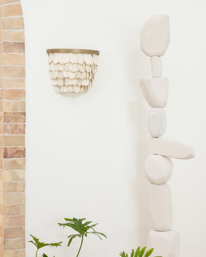 Handmade ceramic petal shaped wall sconce on white wall next to tall rock sculpture