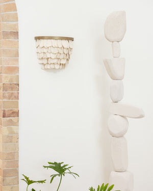 Handmade ceramic petal shaped wall sconce on white wall next to tall rock sculpture