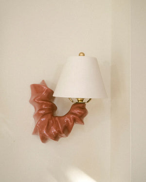 Light red arm shaped matte ceramic wall sconce mounted on white wall