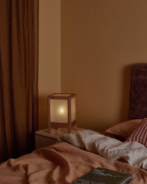 Bedroom with warm interior with a single handmade timber table lamp on a bedside table