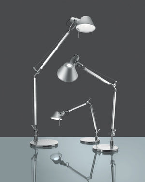 Three adjustable silver metal task lamps with conical shades and circular bases, arranged on a reflective surface against a dark gray background.