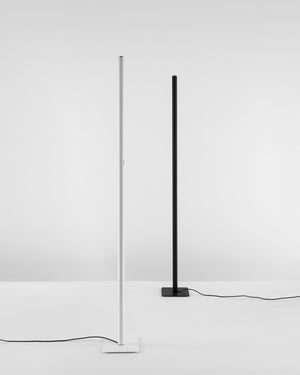 Two minimalist floor lamps with slim vertical poles and square bases, shown on a clean white studio background. One lamp is white and the other is black, both with visible power cords.