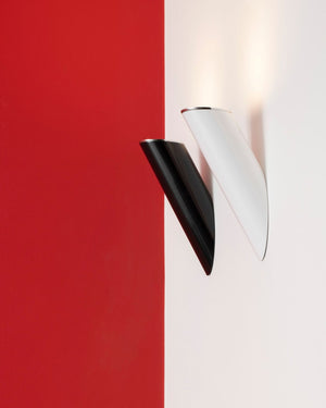 Two modern wall sconces mounted on a split red and white wall, one in glossy black and one in glossy white, with both casting a warm light upward.