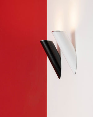 Two modern wall sconces mounted on a split red and white wall, one in glossy black and one in glossy white, with both casting a warm light upward.