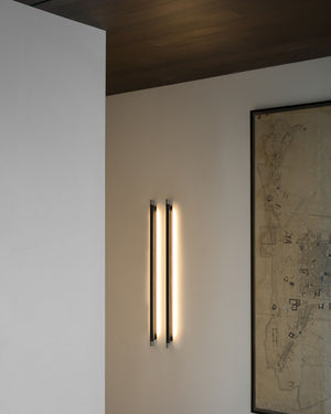 Modern wall-mounted light fixture on a white wall with a framed map in the background.