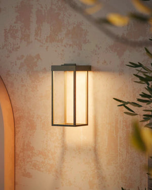 Italian Made Outdoor Lantern Wall Light in antique brass illuminated on textured exterior wall at evening with foliage