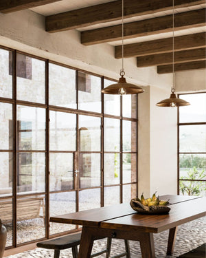 Two Italian brass and copper pendant light displayed in a dining room with windows offering a view on the outside 