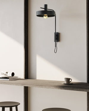 Modern wall-mounted light fixture on a neutral wall with a wooden desk and coffee cup.