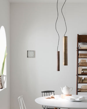 Two tubular pendants with antique iron and brass finishes hanging over a dining table