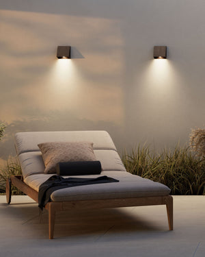 Two square dark brass wall lights when the sun sets down near a sun bed on a terrace