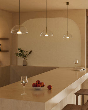 Modern kitchen with pendant lights, a countertop with apples and wine glasses, and a vase.